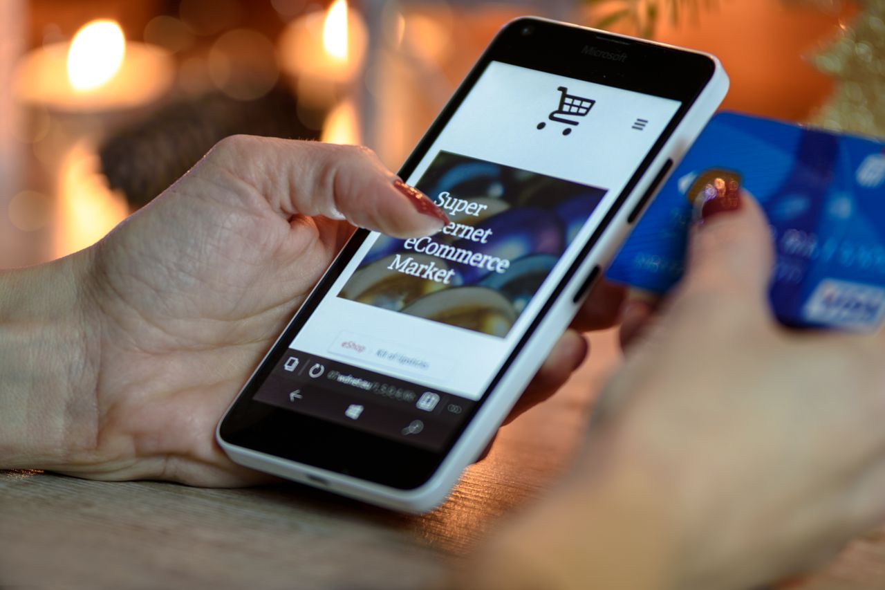 our-story Woman using smartphone for online shopping with credit card in hand, festive background lighting.